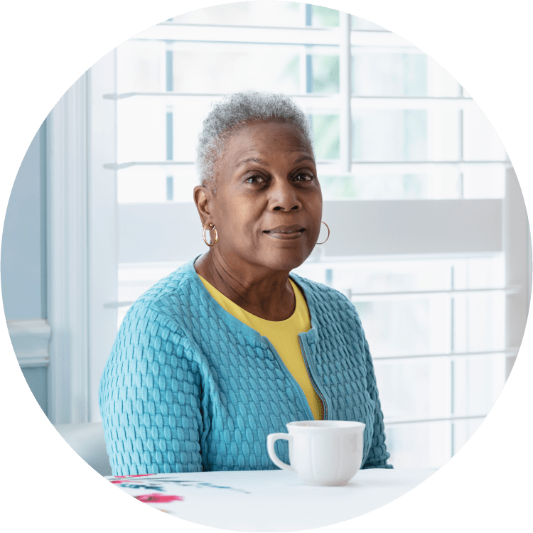 a black senior-aged woman sits at her kitchen table with a cup of coffee on the table.